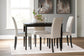 A modern dining room with the Kimonte Rectangular Dining Room Table in dark brown, four beige upholstered chairs, a white rug, minimalist decor, and abstract art on gray walls.