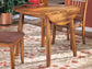 The Berringer Round DRM Drop Leaf Table with two chairs stands on a floral rug, set with dishes in a sunlit room.