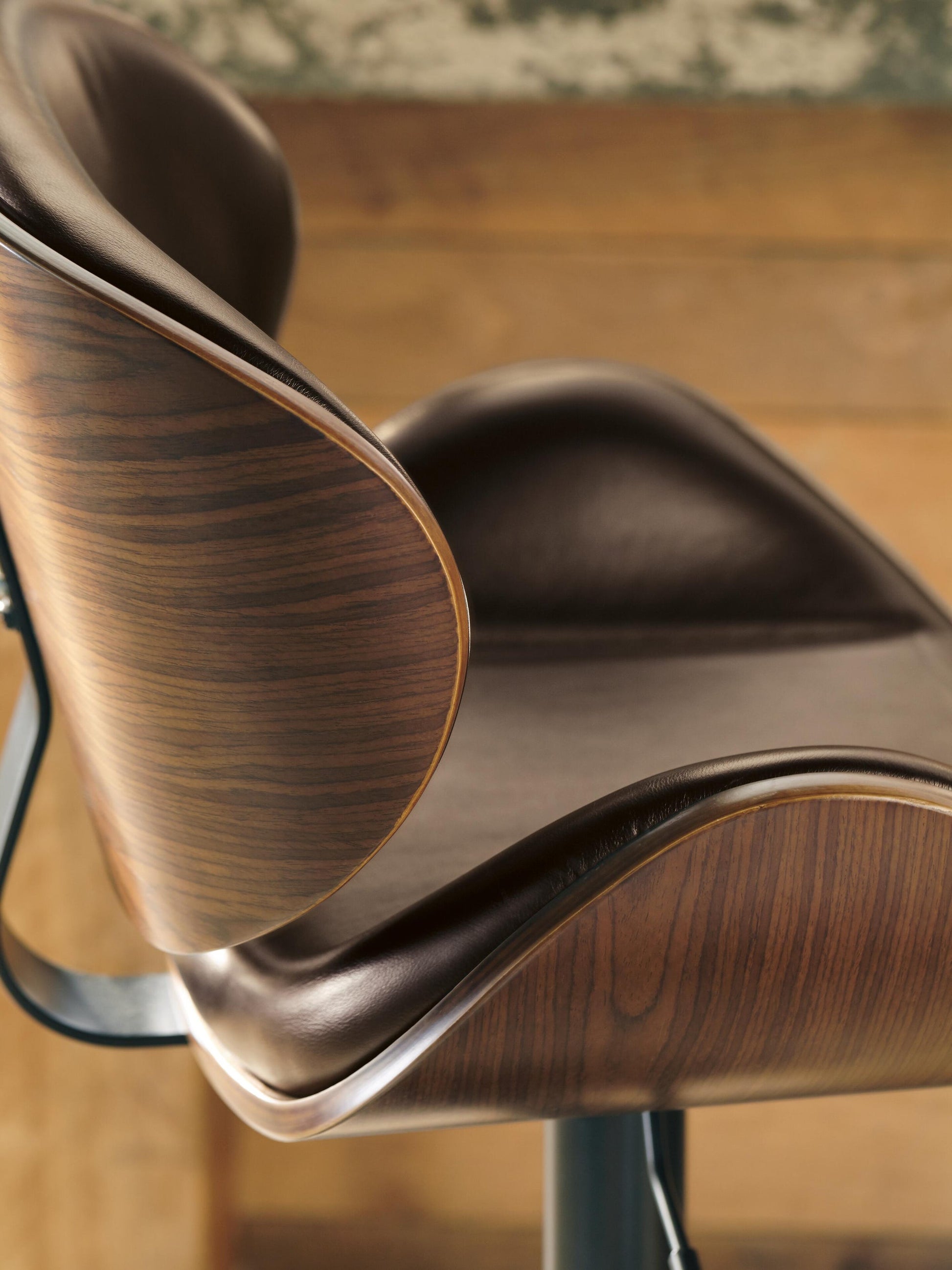 Close-up side view of the Bellatier Tall UPH Swivel Barstool, featuring a curved wood veneer backrest and brown faux leather upholstery, set against a wooden background.