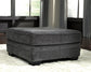 The Tracling Oversized Accent Ottoman in slate gray fabric sits on a white rug in a living room with large windows and gray curtains, enhancing the contemporary style.