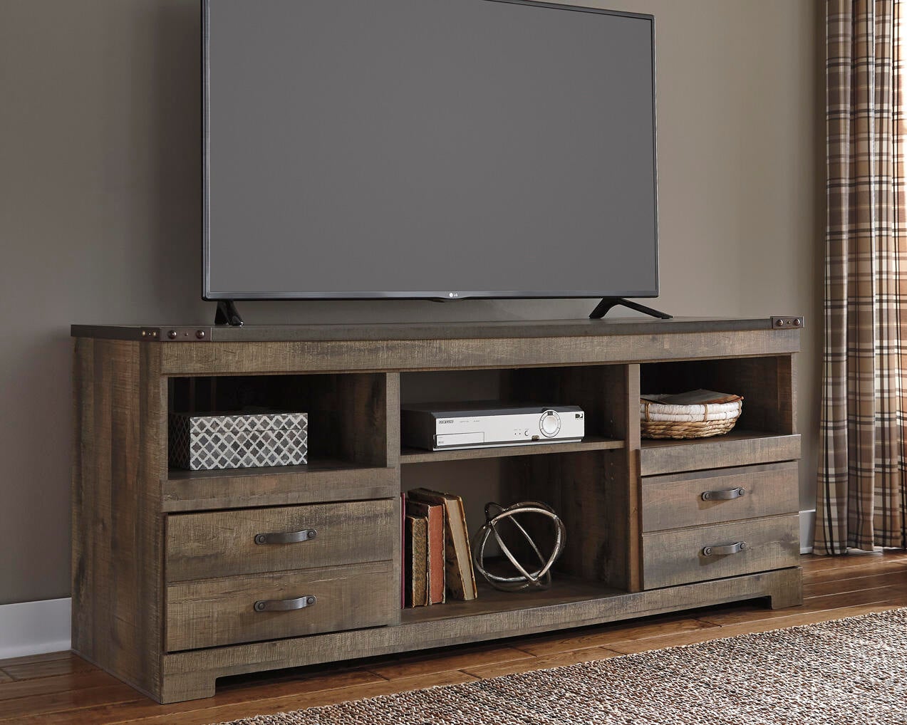 A flat-screen TV sits on the Trinell LG TV Stand w/Fireplace Option, featuring open shelves, drawers, and decor items; plaid curtains hang to the right.