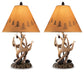 The Derek Poly Table Lamp (set of 2) features antler and pinecone details with tan lampshades showcasing tree silhouettes, adding a cozy mountain retreat style to any room.