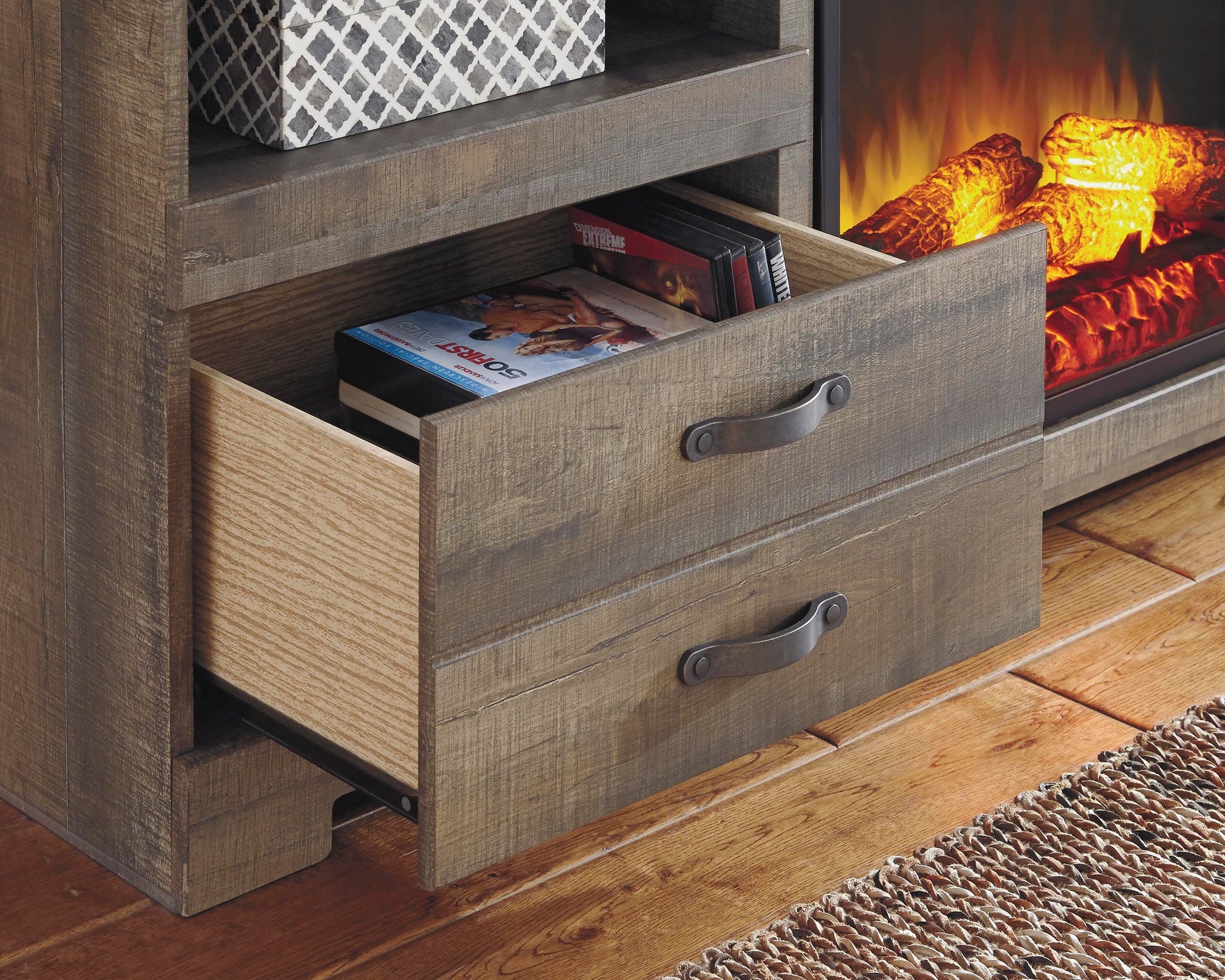 The Trinell LG TV Stand w/Fireplace Option, featuring an open drawer with DVDs and an electric fireplace with artificial flames, creates a cozy focal point.