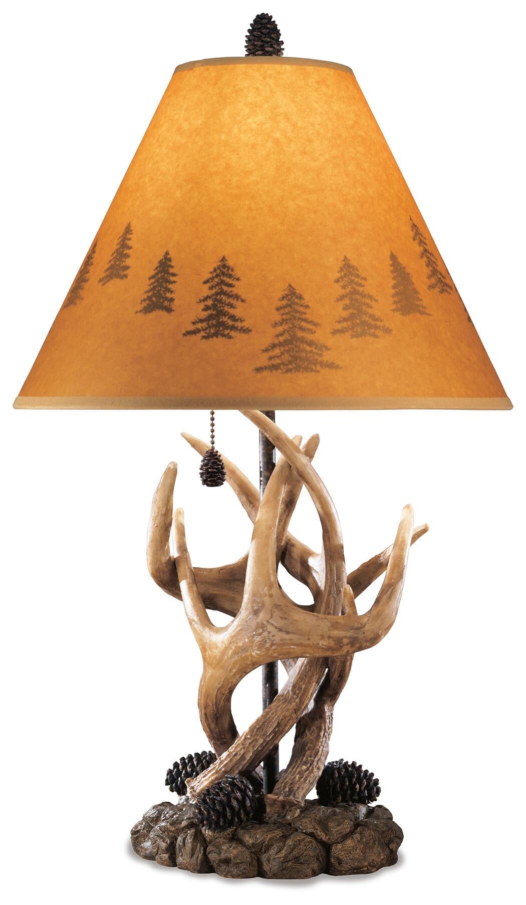 The Derek Poly Table Lamp (2/CN) features an antler-inspired base, pine cone accents, and a tan shade with dark tree silhouettes—an ideal choice to bring mountain retreat style to your space.