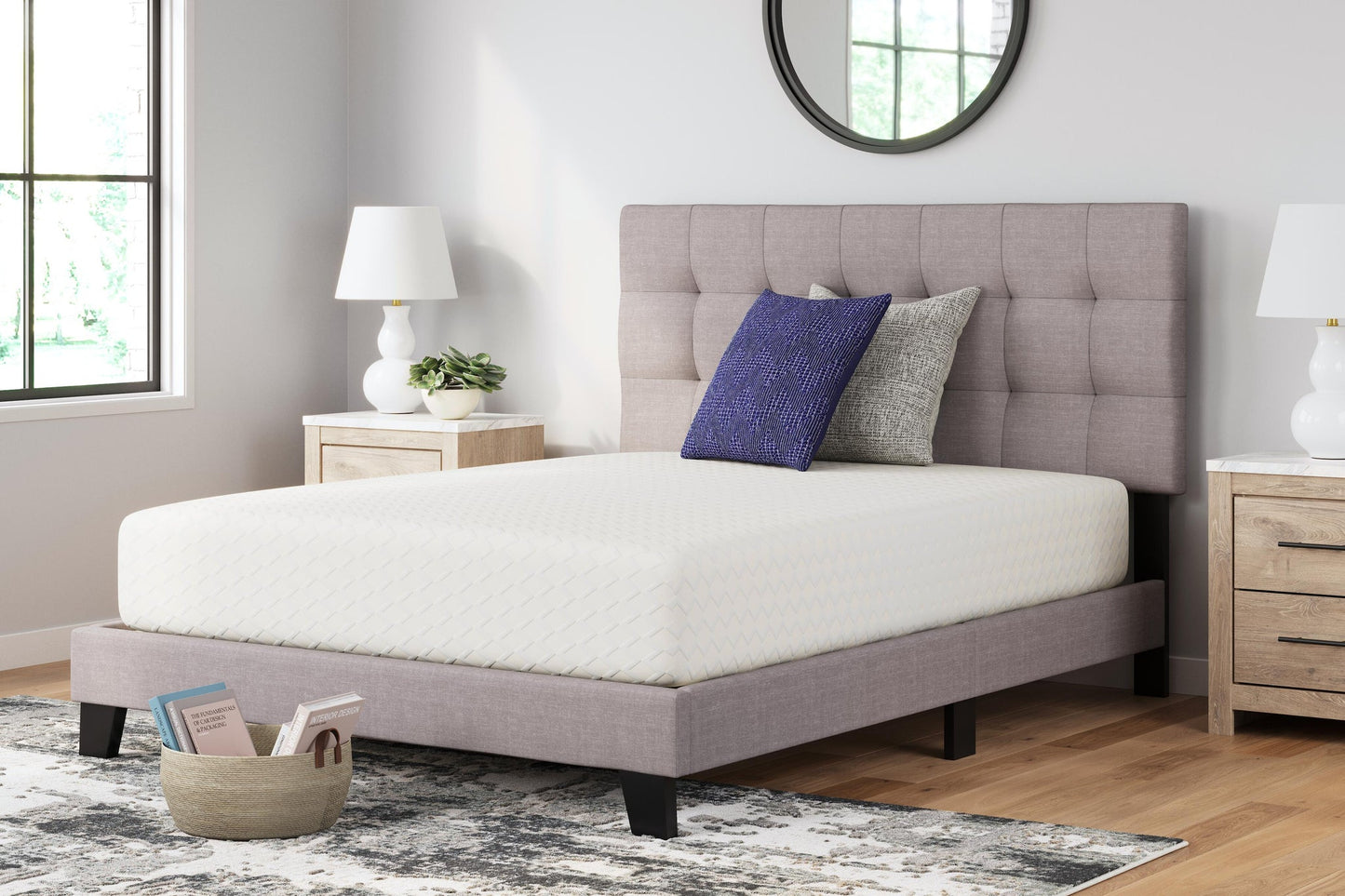 A bright, modern bedroom features a neatly made twin bed with a tufted headboard, two pillows, and nightstands with lamps. Beside the bed sits a basket of books on the floor next to the plush Chime 12 Inch Memory Foam Mattress.