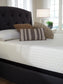 A neatly made bed features a Chime 12 Inch Memory Foam Mattress (queen, white patterned) in a box, three decorative pillows, a headboard, and a bedside table with a lamp and potted plant.