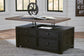 The Tyler Creek Lift Top Cocktail Table, featuring storage drawers, holds an open book and a metal wheel, and is set on a checkered rug in a bright room.