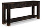 The Gavelston Sofa Table features a weathered black finish, dark wood construction, four drawers, and an open lower shelf for added primitive charm.