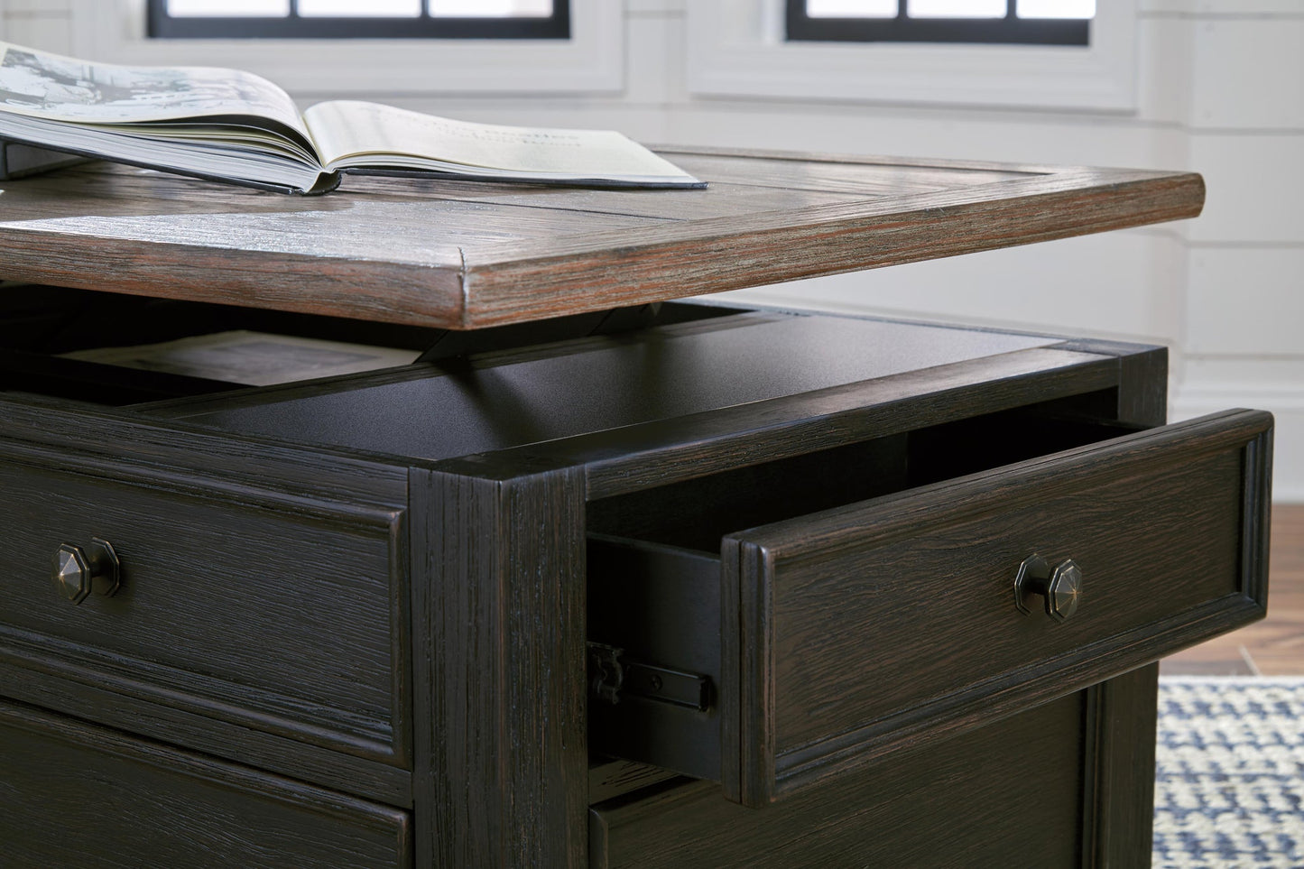 The Tyler Creek Lift Top Cocktail Table features a dark wood finish, a lift-top surface perfect for reading, an open drawer, and spacious storage compartments underneath.