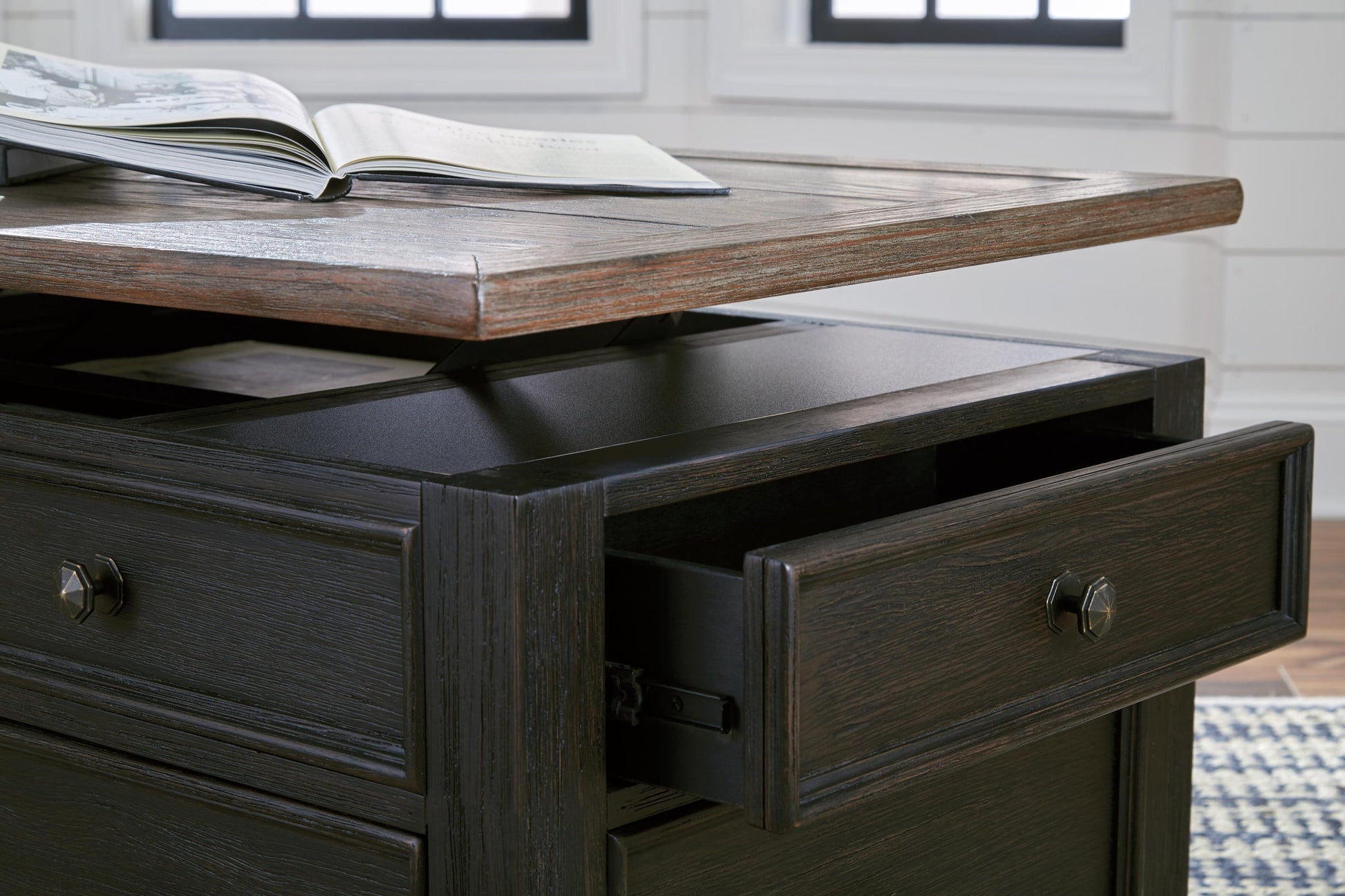 The Tyler Creek Lift Top Cocktail Table features a dark wood finish, a lift-top surface perfect for reading, an open drawer, and spacious storage compartments underneath.