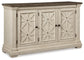 The Bolanburg Dining Room Server is a vintage-inspired wooden sideboard with a weathered oak finish, dark top, and three cream-colored paneled doors featuring a crisscross design and round knobs.