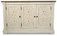 The Bolanburg Dining Room Server is a cream-colored wooden buffet with three paneled doors featuring geometric details and black knobs, a dark wood top, and a weathered oak finish—ideal as a dining room server.