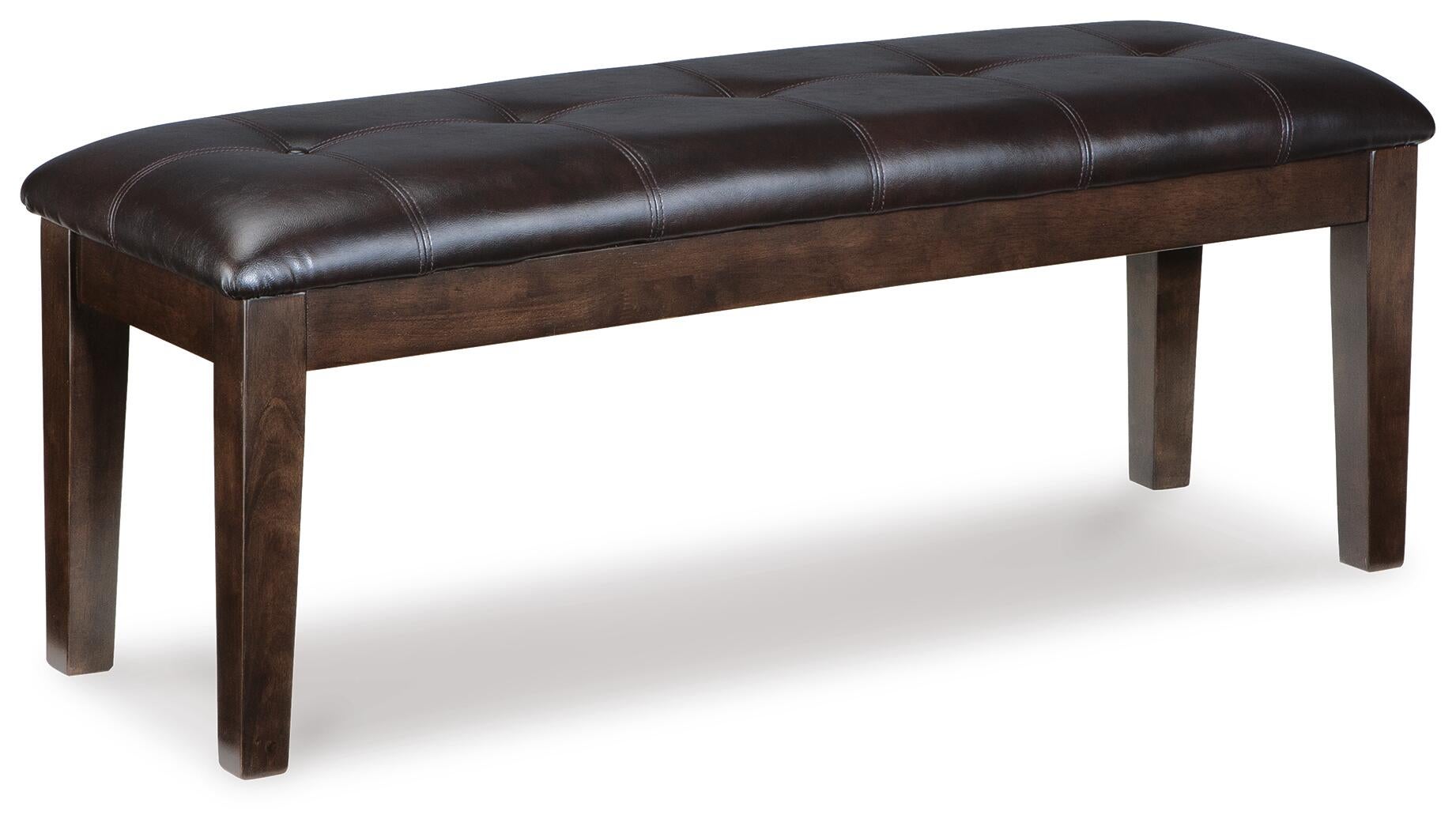 The Haddigan Large UPH Dining Room Bench features a dark brown tufted faux leather seat and wooden legs, set against a white background.
