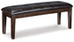 The Haddigan Large UPH Dining Room Bench features a dark brown tufted faux leather seat and wooden legs, set against a white background.