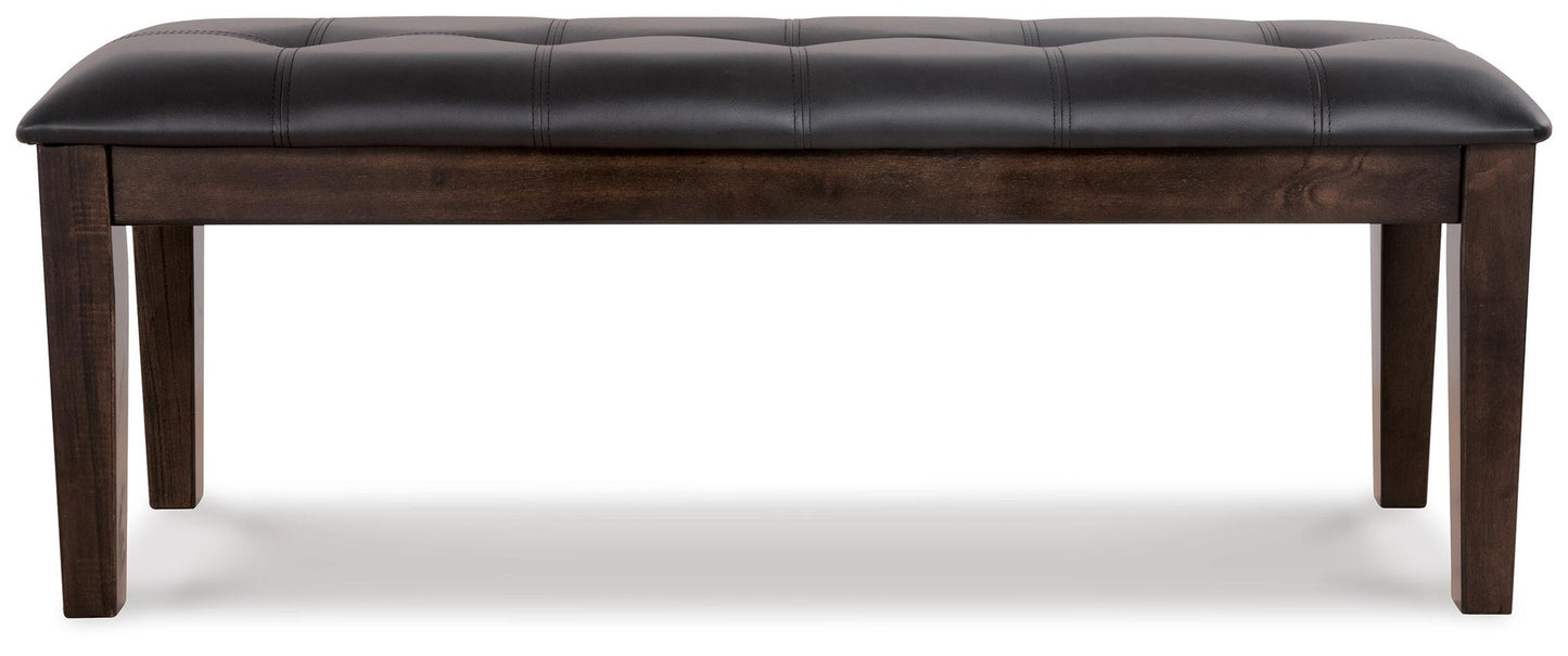 The Haddigan Large UPH Dining Room Bench features a rectangular wooden frame with four legs and a padded, black tufted faux leather seat.
