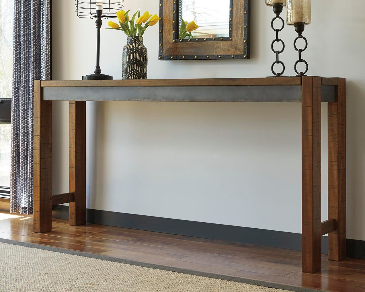 The Torjin Long Counter Table with metallic trim stands against a wall, decorated with yellow tulips, candles, and a framed mirror above it.