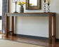 The Torjin Long Counter Table with metallic trim stands against a wall, decorated with yellow tulips, candles, and a framed mirror above it.