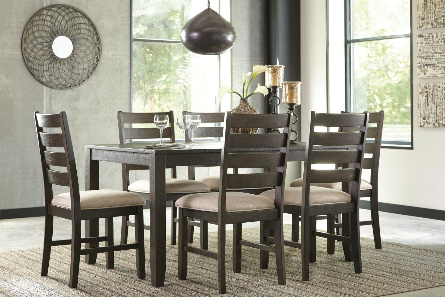 A modern dining room features the Rokane Dining Room Table Set (7/CN) with a wood table, six cushioned upholstered chairs, tableware, decor accents, and a woven rug near large windows.