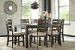 A modern dining room features the Rokane Dining Room Table Set (7/CN) with a wood table, six cushioned upholstered chairs, tableware, decor accents, and a woven rug near large windows.