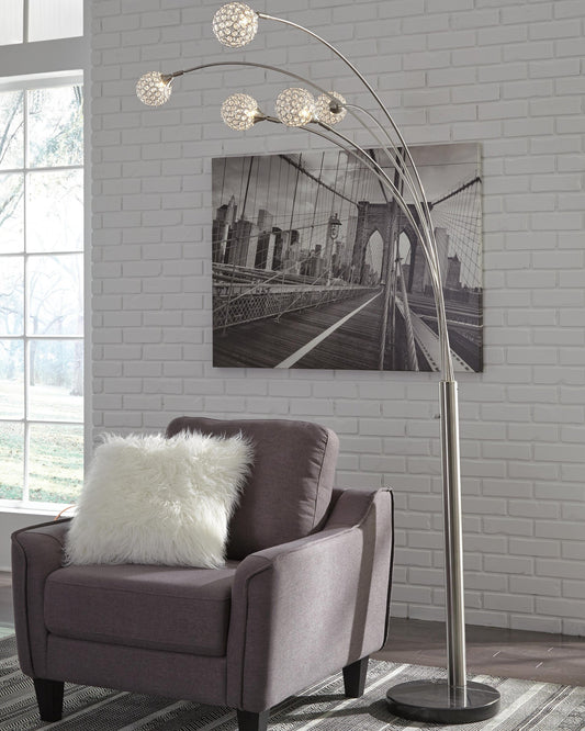 A gray armchair with a white fluffy pillow sits next to the Winter Metal Arc Lamp, featuring five lights and crystal acrylic balls, in front of a black-and-white Brooklyn Bridge photo on a white brick wall.