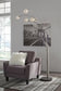 A gray armchair with a white pillow sits beside the Winter Metal Arc Lamp and a black-and-white bridge photo on a white brick wall in a bright room.
