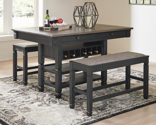 The Tyler Creek RECT Dining Room Counter Table with wine storage and two benches, in dark wood, is styled with decor on a patterned rug in a bright dining nook for cozy urban farmhouse charm.