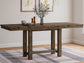The Moriville RECT DRM Counter EXT Table, topped with a vase of branches, dishes, and salt and pepper shakers, stands on a plaid rug in a bright room.