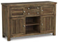 The Moriville Dining Room Server features a rustic distressed nutmeg finish, antiqued bronze-tone hardware, two cabinets, three drawers, and an open central shelf.