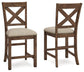 The Moriville Upholstered Barstool (2/CN) set features two wooden barstools with X-shaped backrests, cushioned beige seats, and a distressed nutmeg finish, shown from front and side angles against a white background.