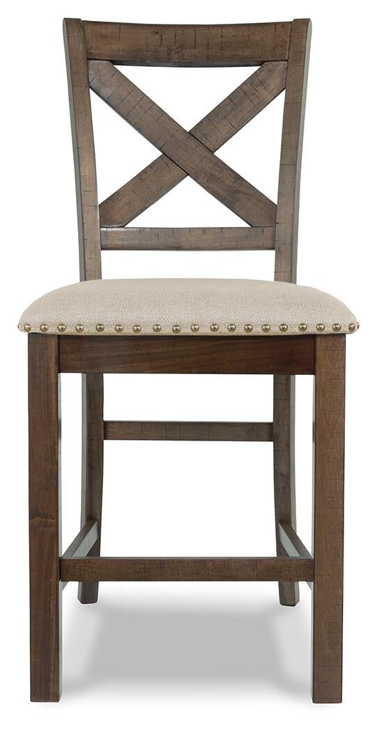 Moriville Upholstered Barstool (2/CN) features a wooden frame, "X" backrest, beige upholstered seat, brass nailhead trim, and a distressed nutmeg finish. Displayed from the front on a white background.