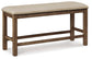 The Moriville Double UPH Bench (1/CN) is a counter height upholstered bench featuring a distressed nutmeg finish, light beige cushion, antiqued nailhead trim, simple rectangular design, and four legs with horizontal supports.