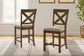 Two Moriville Upholstered Barstools with a distressed nutmeg finish and X-back design feature padded seats and are placed on a patterned rug in a bright room with a window and framed wall art.