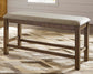 The Moriville Double UPH Bench, featuring a cushioned seat and antiqued nailhead trim, stands on a patterned rug in a bright room.