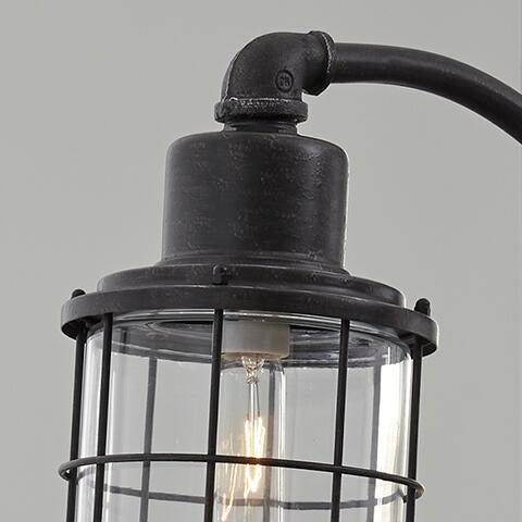 Close-up of the Jae Metal Desk Lamp (1/CN), featuring a black industrial-chic design with a protective metal cage and exposed bulb, highlighting its retro-inspired look against a plain gray background.