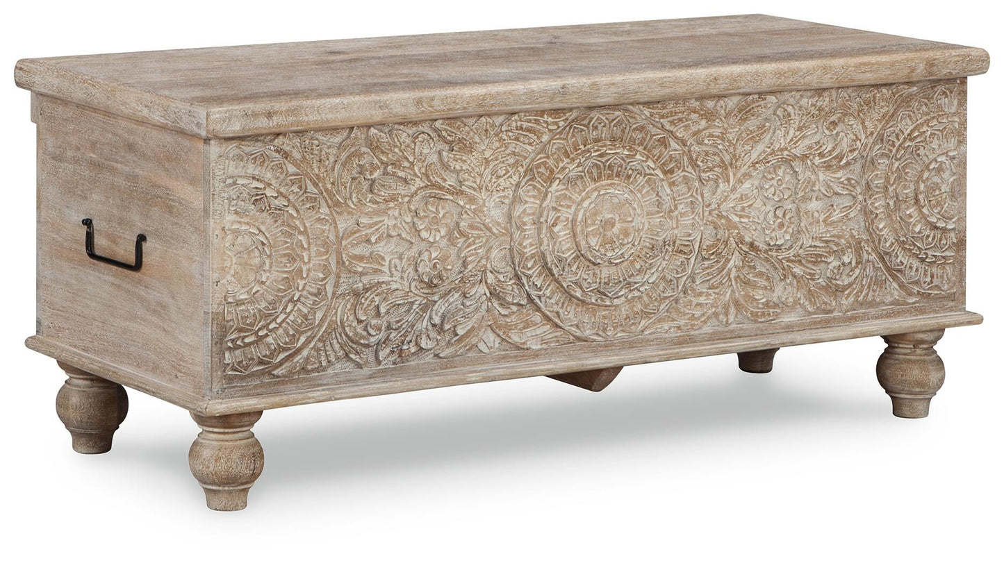 The Fossil Ridge Storage Bench features hand-carved wood, an antique white finish, ornate front floral patterns, metal side handles, and short turned legs.