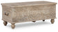 The Fossil Ridge Storage Bench features hand-carved wood, an antique white finish, ornate front floral patterns, metal side handles, and short turned legs.