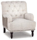 The Tartonelle Accent Chair features a light beige linen weave fabric, button-tufted back, rolled arms, nailhead trim, and dark wooden legs.