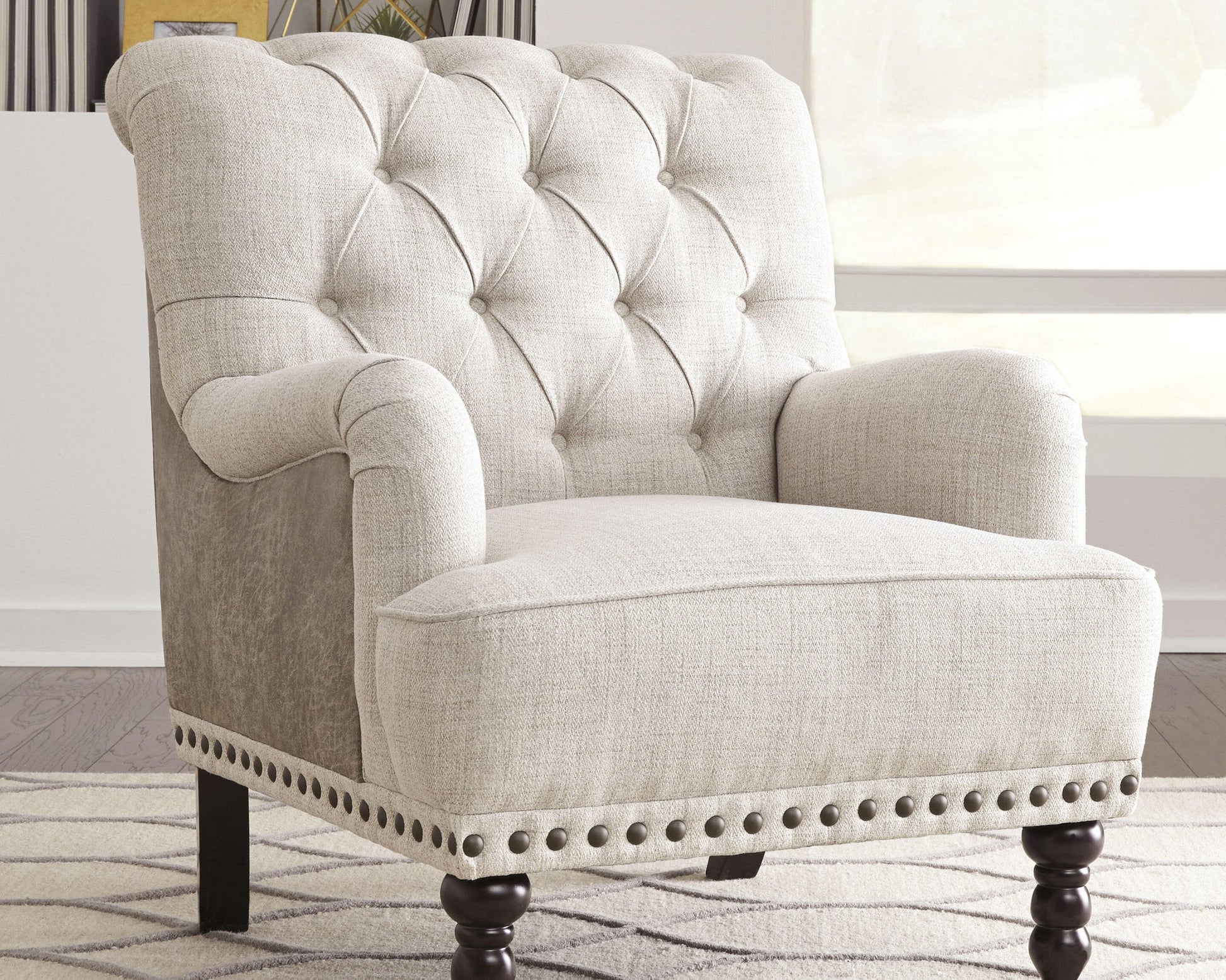 The Tartonelle Accent Chair, featuring button tufting, rolled arms, nailhead trim, and dark wooden legs, sits on a patterned rug in a bright room.
