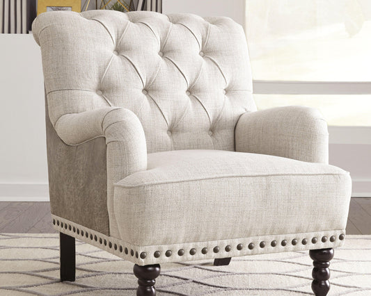 The Tartonelle Accent Chair, featuring button tufting, rolled arms, nailhead trim, and dark wooden legs, sits on a patterned rug in a bright room.