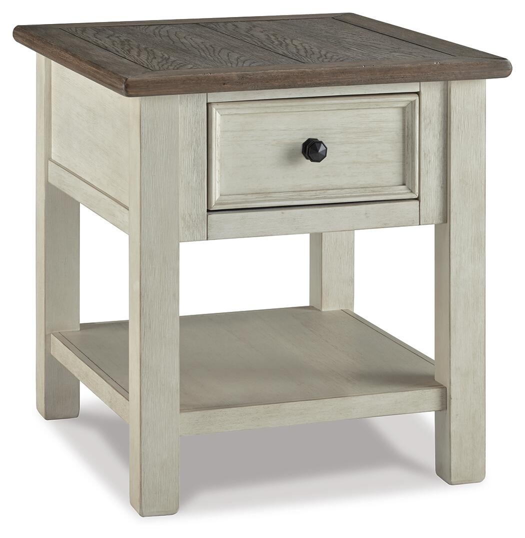 The Bolanburg Rectangular End Table features a two-tone distressed finish with a dark-stained top, light beige body, smooth-gliding drawer with black knob, and an open lower shelf that adds charm to any space.