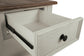 A close-up of the Bolanburg Rectangular End Table’s wooden drawer, partially open, reveals its two-tone distressed finish, black metal handles, and visible sliding hardware.