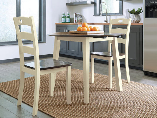 The Woodanville Round DRM Drop Leaf Table with two chairs sits on a woven rug, topped with a tray of oranges, adding a cozy touch to this modern kitchen setting.