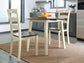 The Woodanville Round DRM Drop Leaf Table with two chairs sits on a woven rug, topped with a tray of oranges, adding a cozy touch to this modern kitchen setting.