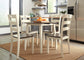 A kitchen featuring the Woodanville Round DRM Drop Leaf Table, four white chairs with dark seats, a bowl of oranges, modern appliances, and a woven rug creates a cozy and inviting space.