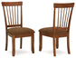 Two Berringer Dining UPH Side Chairs (2/CN) feature wooden frames, vertical slat backs, and brown microfiber upholstery, displayed from front and side angles on a white background.