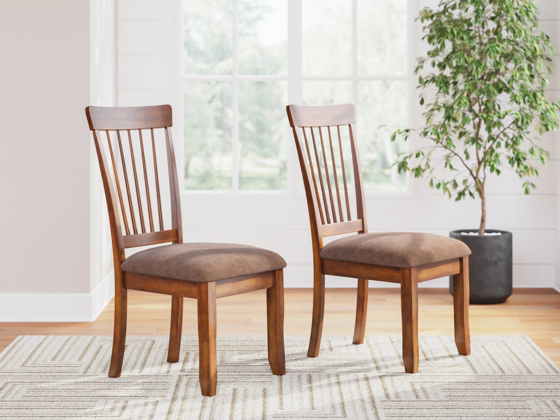 Two Berringer Dining UPH Side Chairs with brown cushioned seats are set on a light patterned rug in a bright room with large windows and a potted plant.