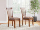Two Berringer Dining UPH Side Chairs with brown cushioned seats are set on a light patterned rug in a bright room with large windows and a potted plant.