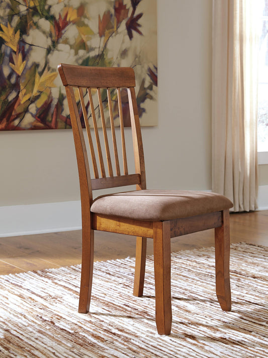 A Berringer Dining UPH Side Chair sits on a patterned rug in a sunlit room, accented by a floral painting and beige curtains in the background.