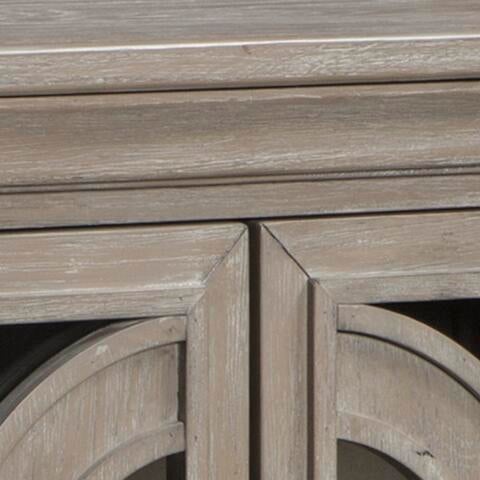Close-up of the Fossil Ridge Accent Cabinet, a 4-door piece with a weathered light brown finish, decorative geometric door details, and adjustable shelves for versatile storage.
