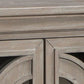 Close-up of the Fossil Ridge Accent Cabinet, a 4-door piece with a weathered light brown finish, decorative geometric door details, and adjustable shelves for versatile storage.